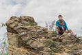 Young man sitting alone on abandoned fortress stone wall with cloudy sky background. Solo traveler concept