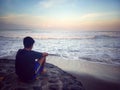 Young man sitting alone on beach from behind at sunset. Royalty Free Stock Photo