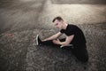 Young man sitting on the asphalt and and stretches his legs before jogging. Running, sports, healthy lifestyle