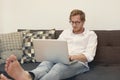 Young man sitting barefoot on couch with laptop Royalty Free Stock Photo