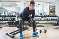 Young man sitting on bench and lifting weights in gym Royalty Free Stock Photo