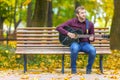 Young man sitting on bench and playing acoustic guitar Royalty Free Stock Photo