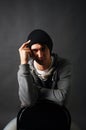 The young man sitting on a chair in a gray hoodie and a black hat holding his hand to his head in the shade Royalty Free Stock Photo