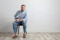 Young man sitting on chair near white brick wall in office, space for text Royalty Free Stock Photo