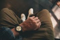 Young man sitting on chair wears a tartan shirt looking at his analog watch on his hand watching the time at the coffee shop.