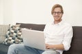 Young man sitting on couch with laptop and smiles Royalty Free Stock Photo