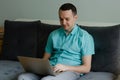 Young man sitting on the couch, thinking and working on laptop Royalty Free Stock Photo