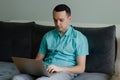 Young man sitting on the couch, thinking and working on laptop Royalty Free Stock Photo