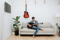 Young man sitting cross-legged on a sofa at home, playing guitar Royalty Free Stock Photo