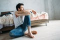 Young man sitting down on the floor near the bed and looking outside Royalty Free Stock Photo