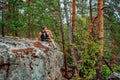 A young man is sitting on the edge of a cliff overlooking a grand panorama of a pristine forest with rocks