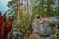 A young man is sitting on the edge of a cliff overlooking a grand panorama of a pristine forest with rocks