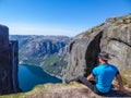 Norway - A man sitting at the egde of a steep mountain with a fjord view