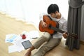 Young man sitting on floor and holding acoustic instrumental guitar playing new written song.