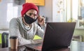 A young man is sitting in front of a laptop screen at home, working remotely and removing a protective face mask Royalty Free Stock Photo