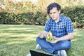 Young man sitting in the grass eating a fresh salad while working on his laptop Royalty Free Stock Photo