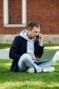 Focused freelancer man sitting on grass with legs crossed remote work on laptop, talk on cellphone. Royalty Free Stock Photo