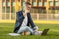 A young man sitting on the grass, talking on a mobile phone, with a laptop Royalty Free Stock Photo