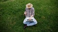 Young man sitting on green grass and working on laptop outdoors, remote work concept Royalty Free Stock Photo