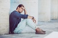 Young man sitting on the ground outdoors with hand in hair. Casual clothes, profile view Royalty Free Stock Photo