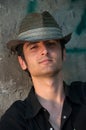 Young man sitting in hat near wall