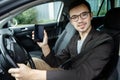 Young man is sitting at his car while looking at the camera. His left hand is on the steering wheel. He is holding the phone in Royalty Free Stock Photo