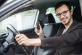 Young man is sitting at his car while looking at the camera. He is holding the keys in his right hand. His left hand is on the Royalty Free Stock Photo