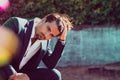 Young man sitting with his hands in his hair and staring. Thoughtful and worried attitude. Outdoors, he is wearing a jacket and a Royalty Free Stock Photo