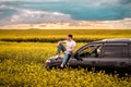 Young man sitting on the hood of a car in the field Royalty Free Stock Photo