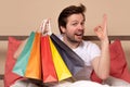 Young man sitting at hte bed at home holding some shopping bags Royalty Free Stock Photo