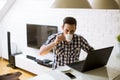 Young man sitting on kitchen desk at home and using laptop and drinking coffee Royalty Free Stock Photo