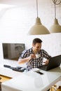 Young man sitting on kitchen desk at home and using laptop and drinking coffee Royalty Free Stock Photo