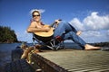 Young Man Sitting Lakeside and Playing Guitar Royalty Free Stock Photo