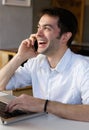 Young man sitting by laptop calling by mobile phone Royalty Free Stock Photo