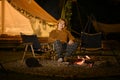 Man sitting near burning campfire and tent in the evening forest. Royalty Free Stock Photo