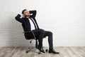 Young man sitting in office chair near white brick wall indoors, space for text Royalty Free Stock Photo