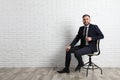 Young man sitting in office chair near white brick wall indoors, space for text Royalty Free Stock Photo