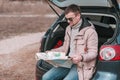 Young man is sitting in open trunk of car near the river and watching road map