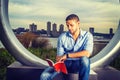 Young man sitting outdoors in New York City, reading red book Royalty Free Stock Photo