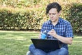 Young man sitting in a park looking at a laptop and opening a reusable bottle