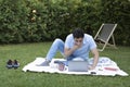 Young man sitting on the picnic blanket and working on laptop on the grass in the park Royalty Free Stock Photo