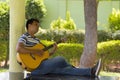 Young man sitting playing guitar under tree Royalty Free Stock Photo