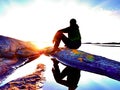 Young man sitting on a rock watching a gorgeous sunset on the sea. Hiker alone enjoy evening