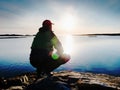 Young man sitting on a rock watching a gorgeous sunset on the sea. Hiker alone enjoy evening