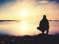 Young man sitting on a rock watching a gorgeous sunset on the sea. Hiker alone enjoy evening