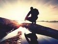 Young man sitting on a rock watching a gorgeous sunset on the sea. Hiker alone enjoy evening