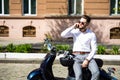 Young man sitting on scooter and using smart phone on city street Royalty Free Stock Photo