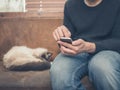 Young man sitting on sofa with cat using his smartphone Royalty Free Stock Photo