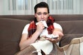 Young man sitting on the sofa with handkerchief in one hand and pills in another looking sick illness at home