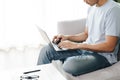 Young man sitting on the sofa at home typing on the laptop keyboard for online working, using internet, freelancer, relaxed,